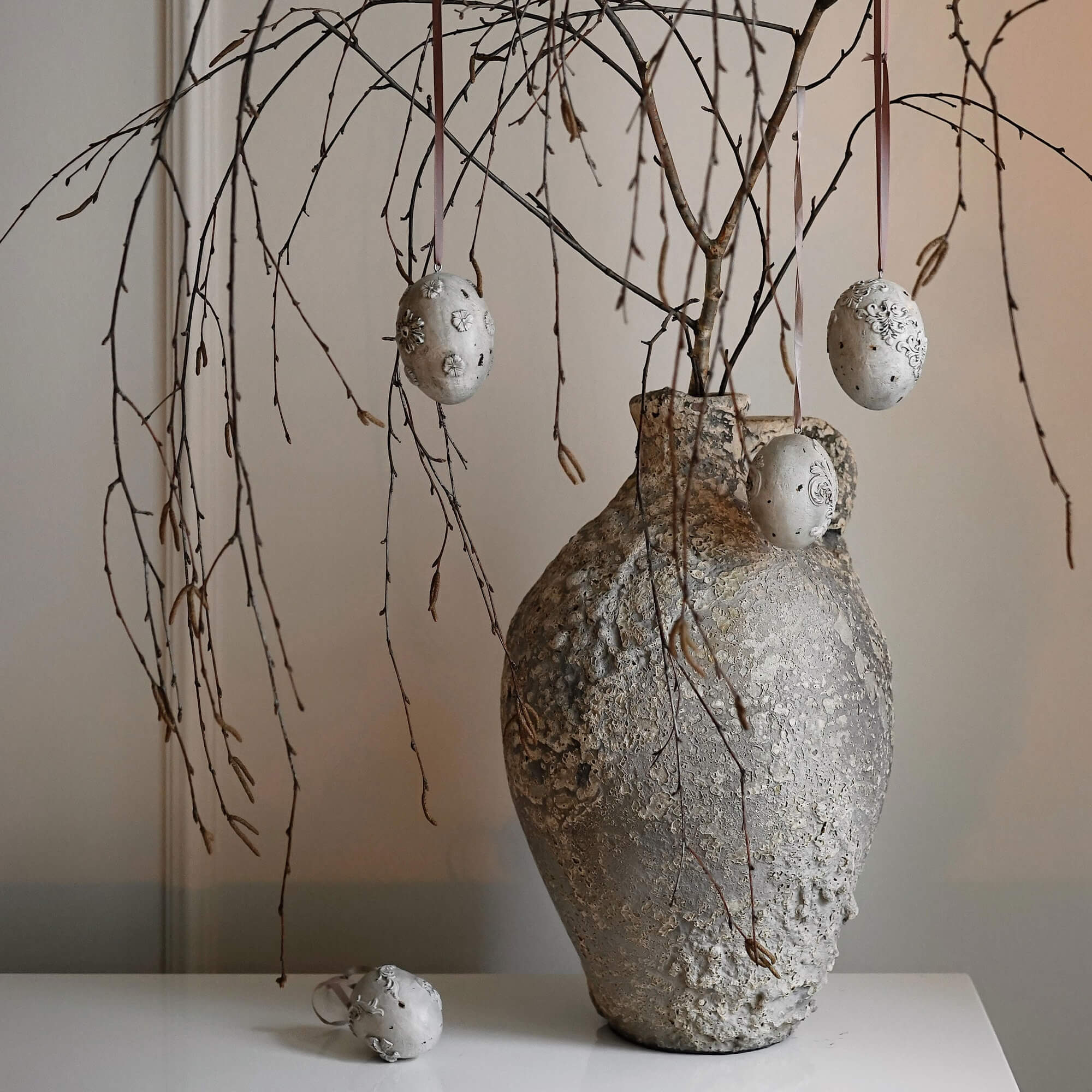 Vaso rustico grigio con texture, rami e decorazioni sospese a forma di uova decorative