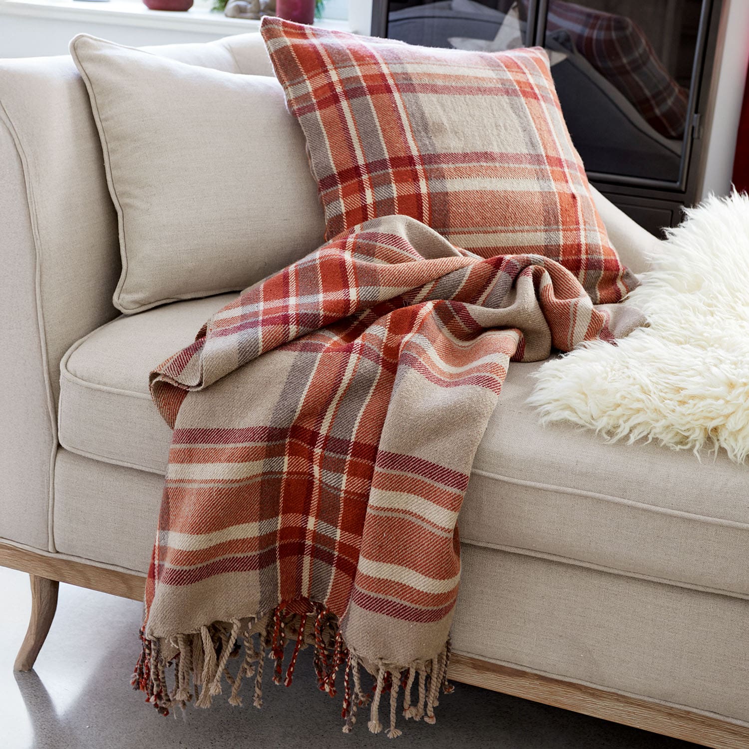 Divano beige con cuscino e plaid a quadri in tonalità rosse e marroni per un soggiorno accogliente