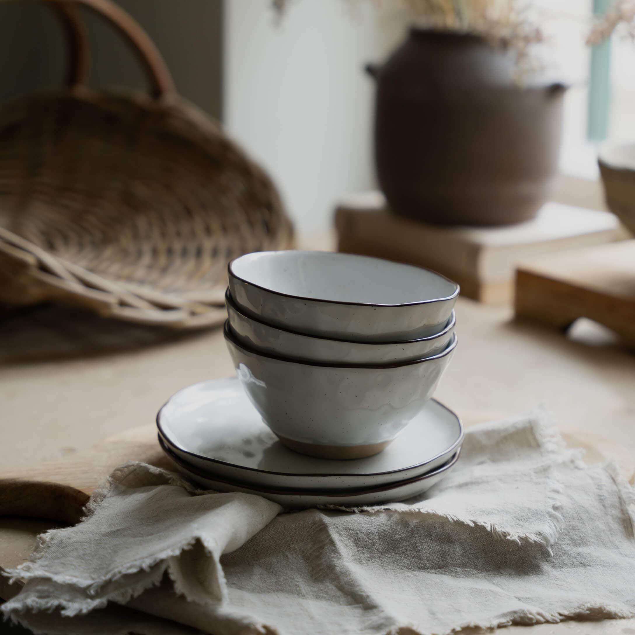 Set di ciotole e piatti in ceramica bianca con bordo nero su tessuto di lino per cucina