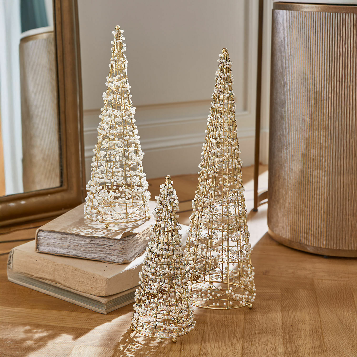 Set di 3 alberi decorativi Amelioro Set di tre coni decorativi in filo dorato con perle bianche su tavolo in legno