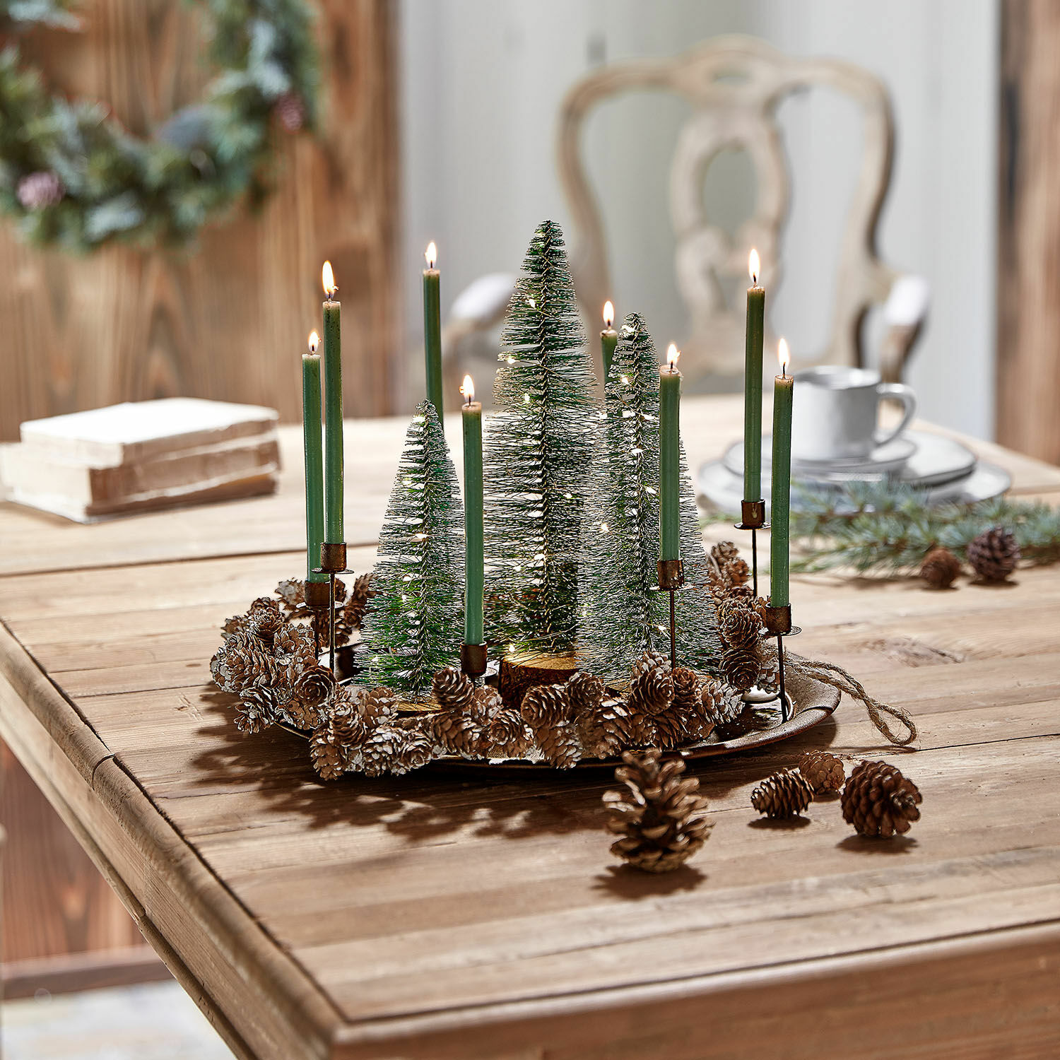 Corona decorativa natalizia con candele verdi e pigne su tavolo in legno