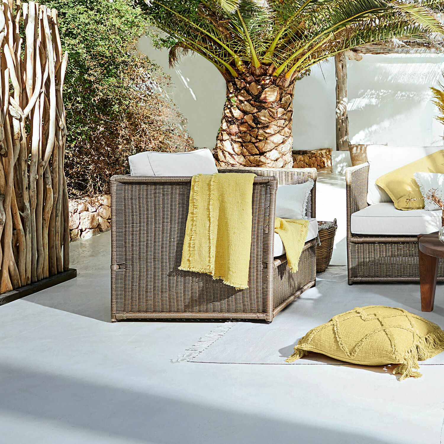 Poltrona Lesmont Set di mobili da giardino in rattan marrone con cuscini bianchi e dettagli gialli su terrazza soleggiata