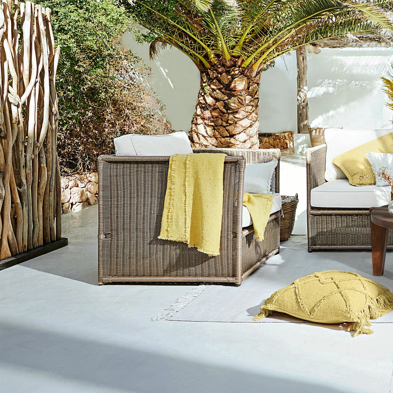 Poltrona Lesmont Set di mobili da giardino in rattan marrone con cuscini bianchi e dettagli gialli su terrazza soleggiata