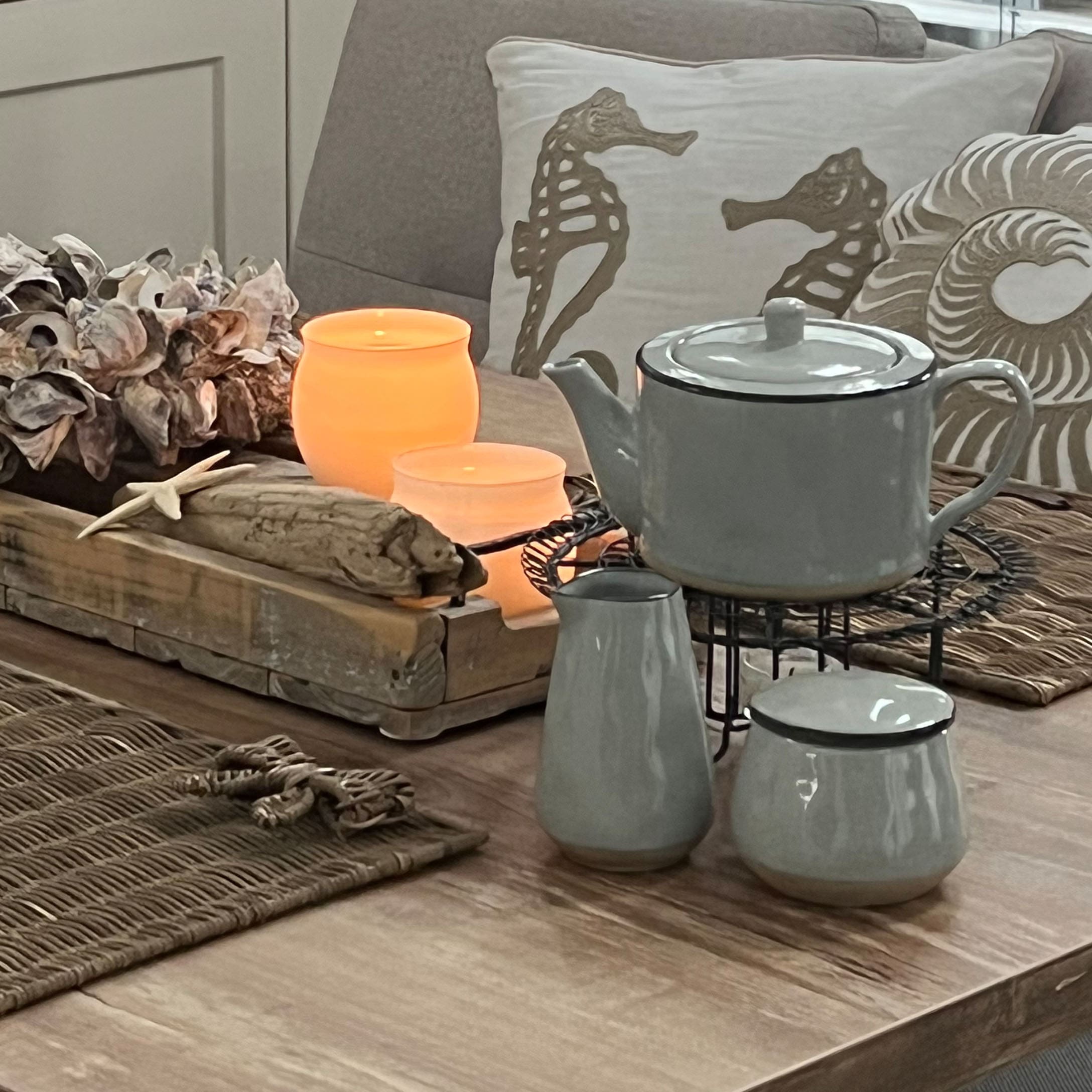Set da tè in ceramica grigia su tavolo in legno con decorazioni marine e candele accese