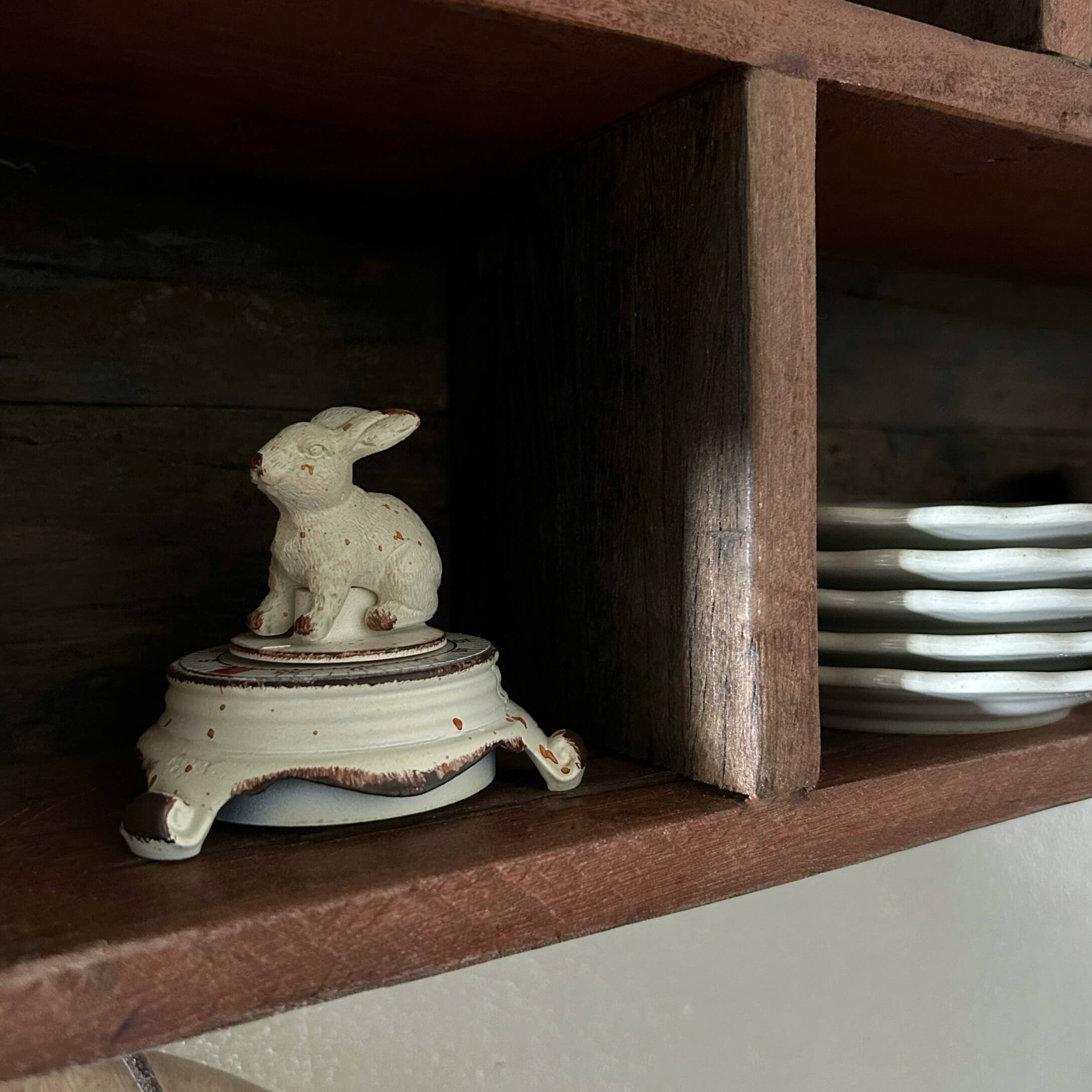 Contenitore in ceramica bianca con coperchio a forma di coniglio su mensola in legno accanto a piatti