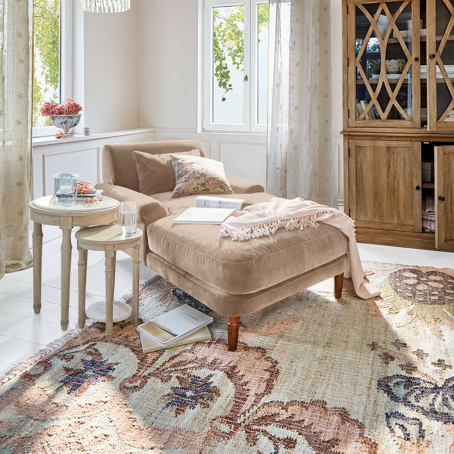 Chaise longue Jouvrelle Chaise longue beige in velluto con cuscini e coperta rosa su tappeto decorato in soggiorno luminoso