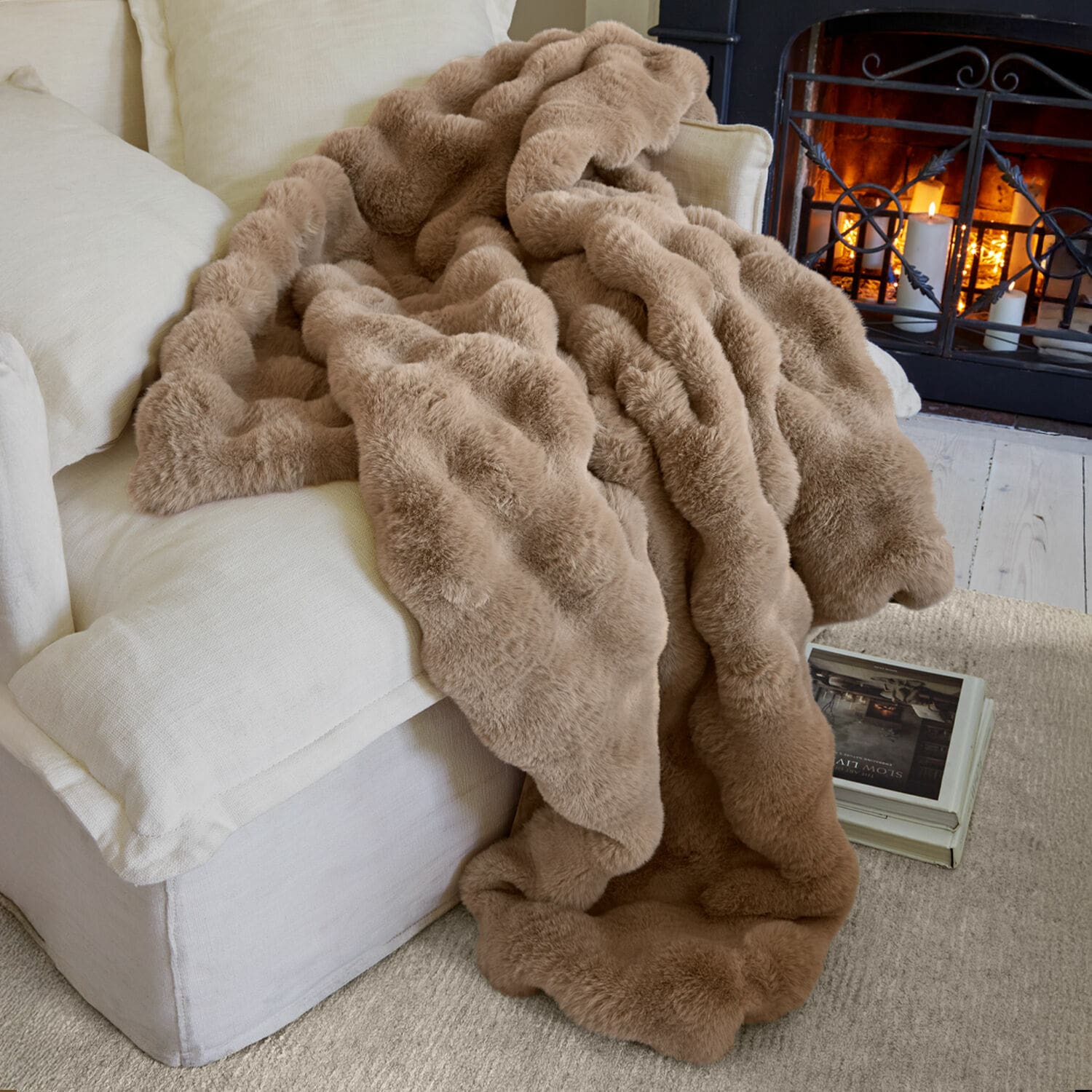 Coperta Zalina Coperta beige in pelliccia sintetica morbida su divano chiaro vicino al camino acceso per comfort