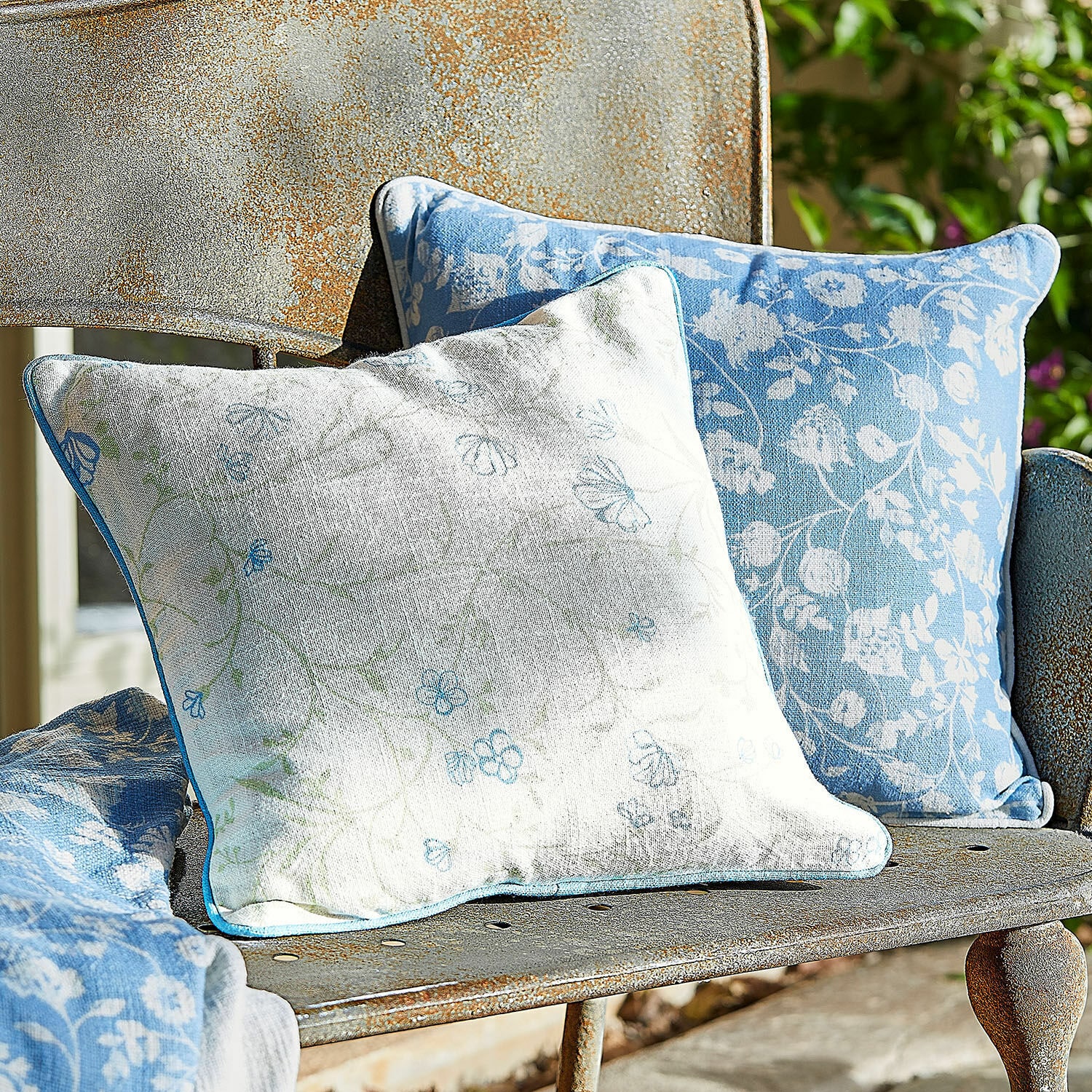 Coppia di copricuscini Corvelique Due cuscini decorativi in cotone blu e bianco con motivo floreale su panchina metallica arrugginita in giardino