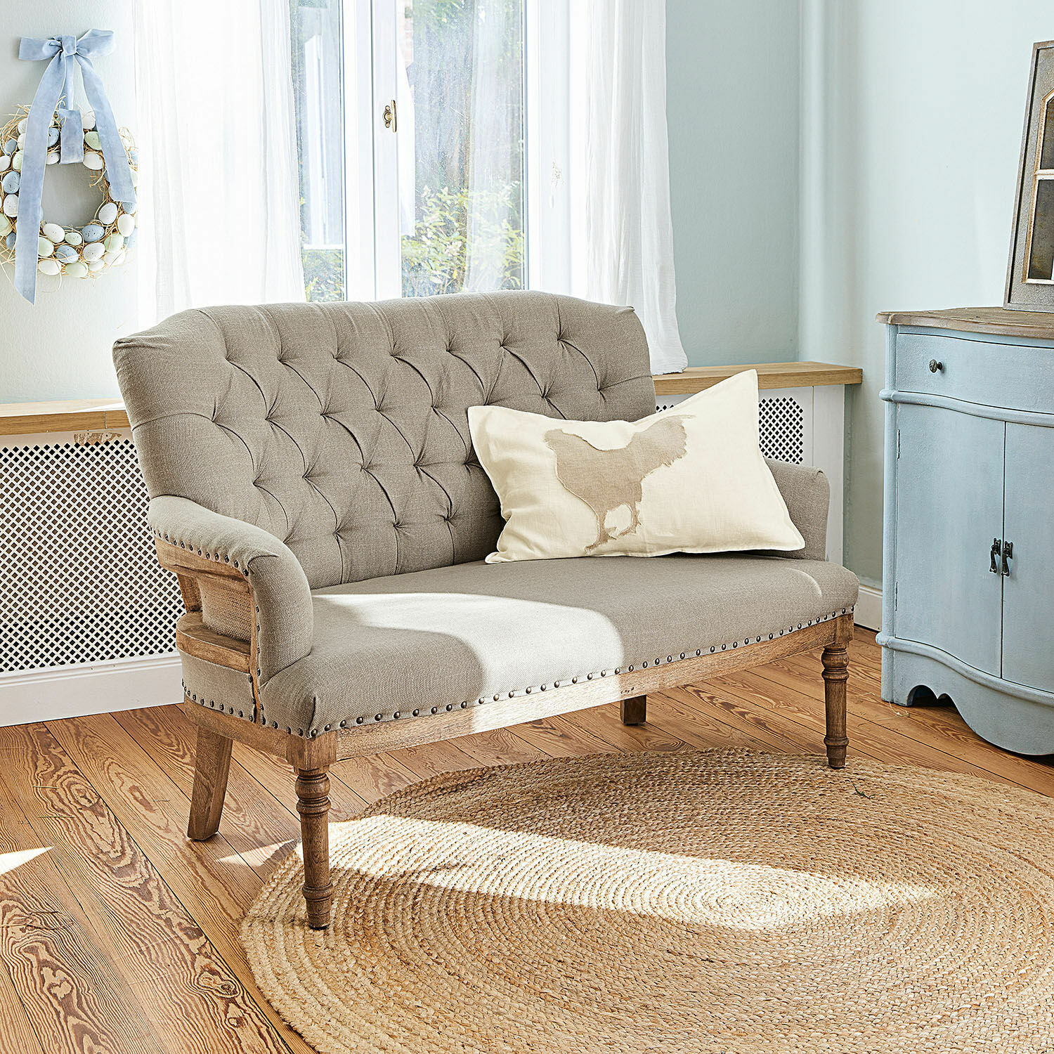 Divano Kingsley Divano beige imbottito con struttura in legno e bottoni decorativi in soggiorno luminoso