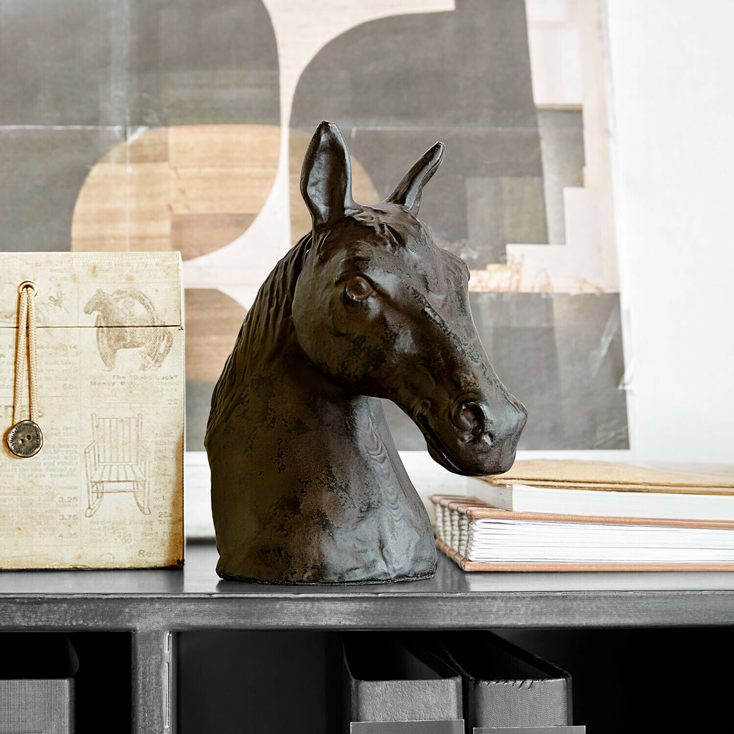 Testa di cavallo decorativa in metallo scuro su mensola con libri e scatola