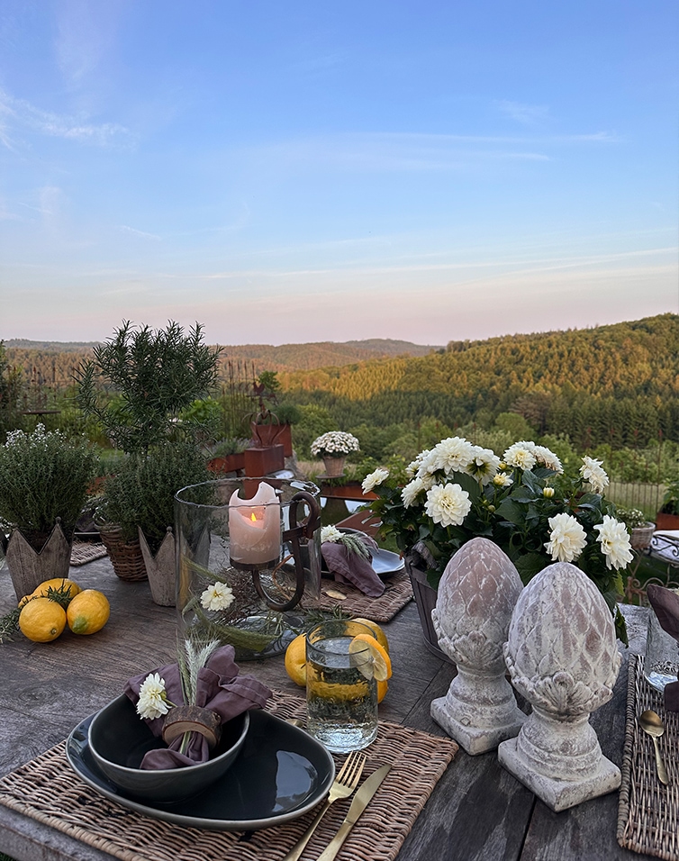 Tavolo rustico con decorazioni in pietra e fiori bianchi davanti a colline verdi e cielo azzurro