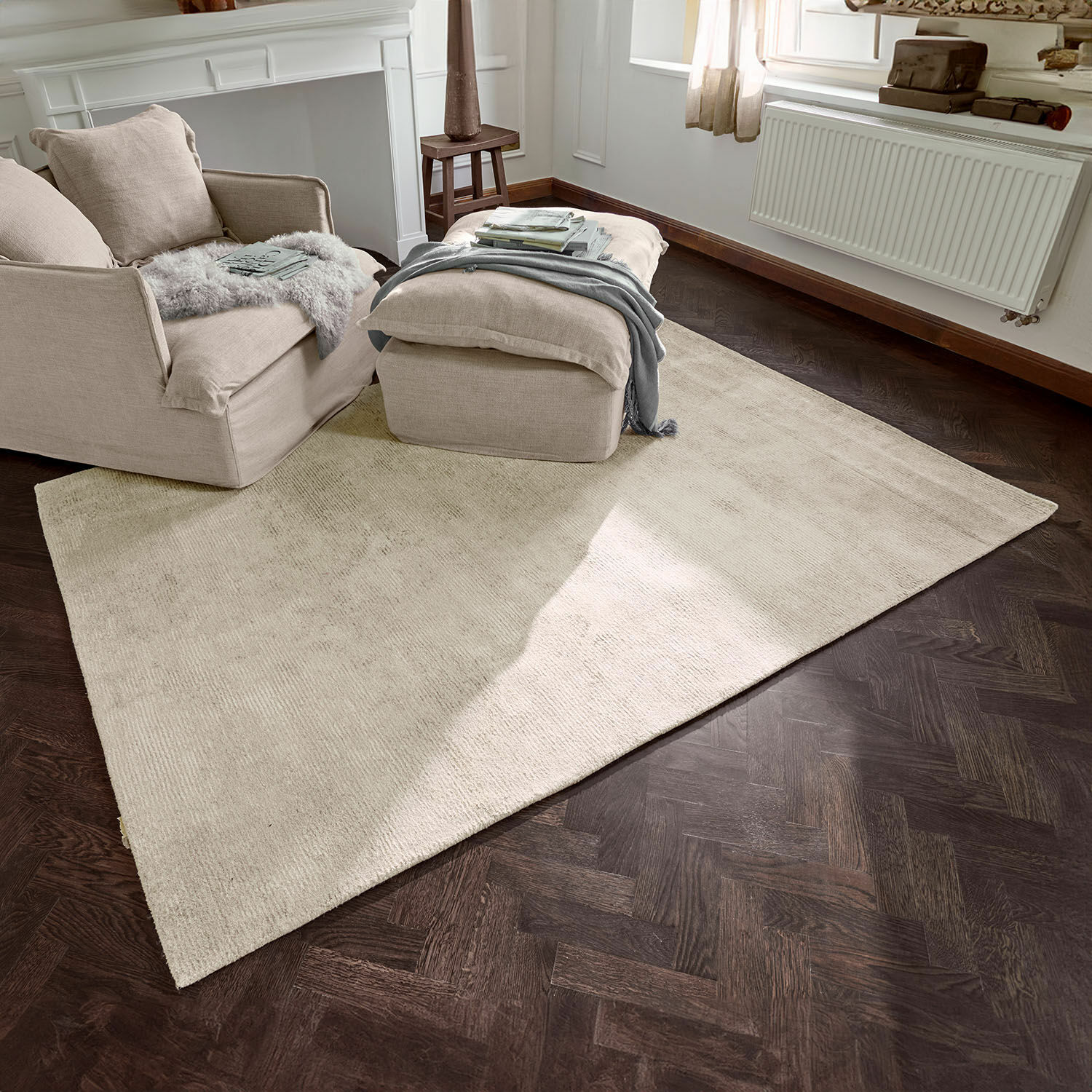 Tappeto Zaniyah Tappeto beige in materiale morbido su pavimento in legno scuro in soggiorno luminoso con poltrona