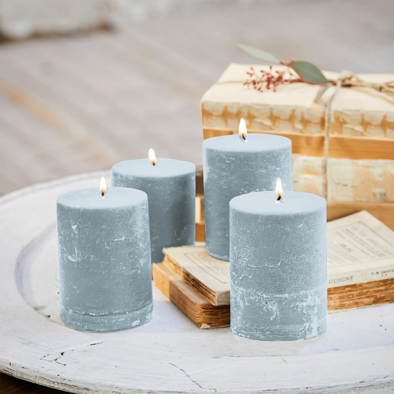 Set di quattro candele blu in cera su tavolo di legno bianco con libri e regalo