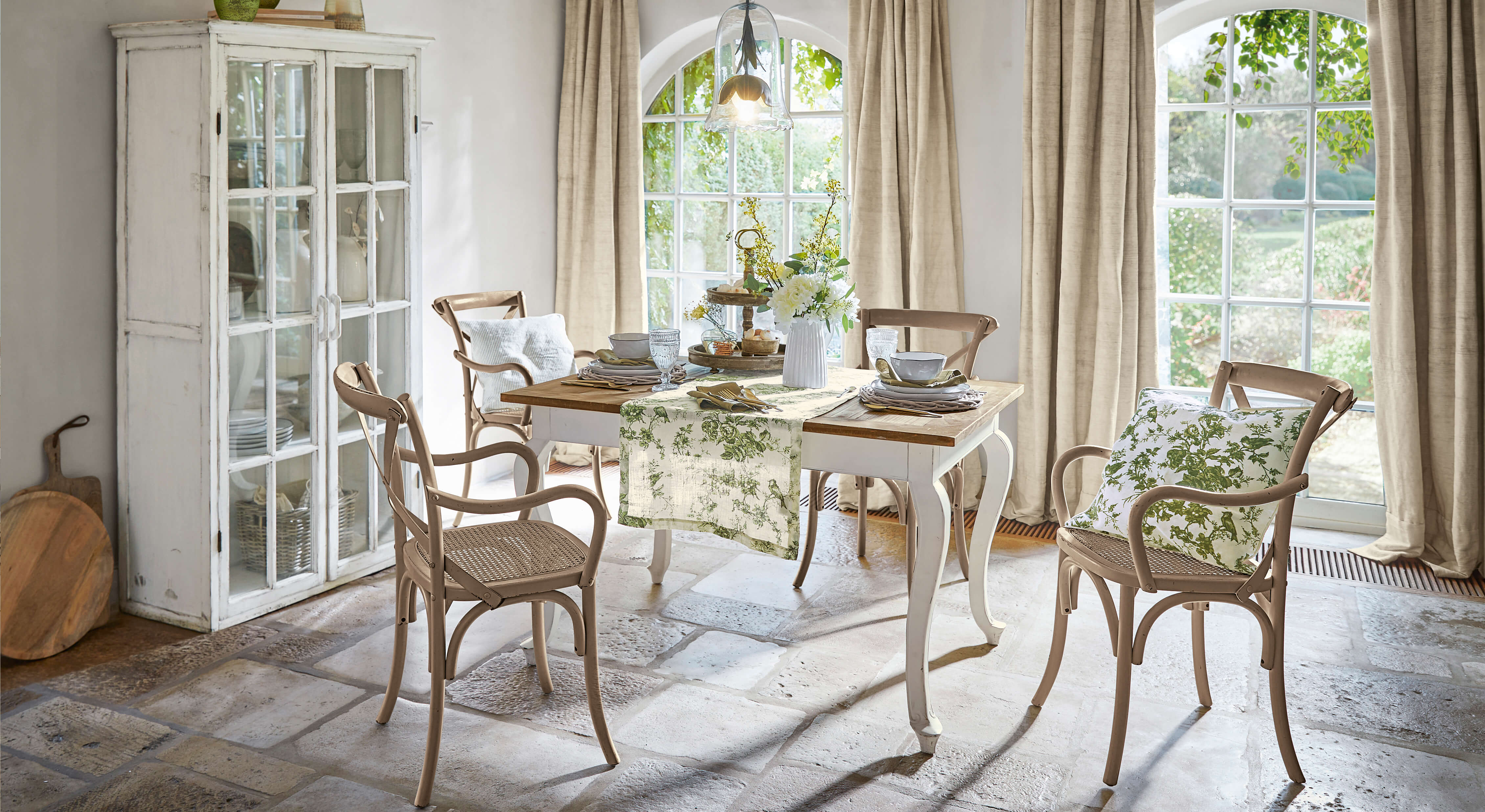 Sala da pranzo con tavolo in legno e sedie beige con cuscini verdi, luce naturale dalle finestre