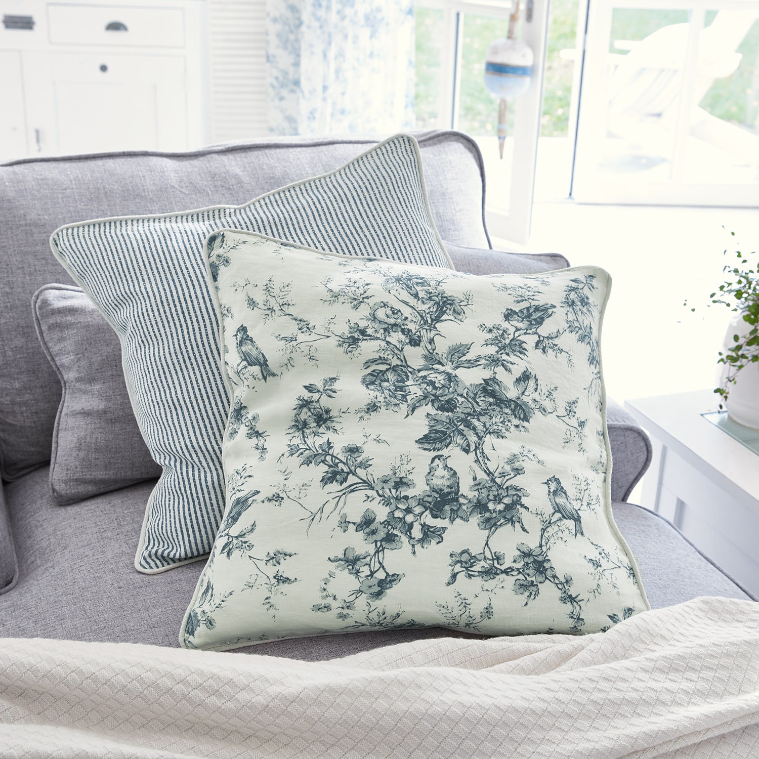 Cuscino decorativo reversibile in cotone con motivi floreali e righe blu su divano grigio