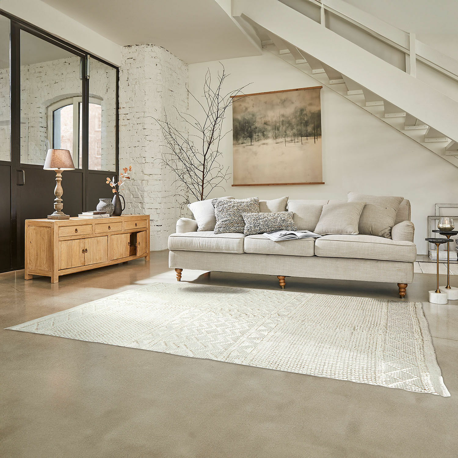 Tappeto Hadir Divano beige con cuscini e credenza in legno chiaro in soggiorno luminoso con tappeto e decorazione a parete