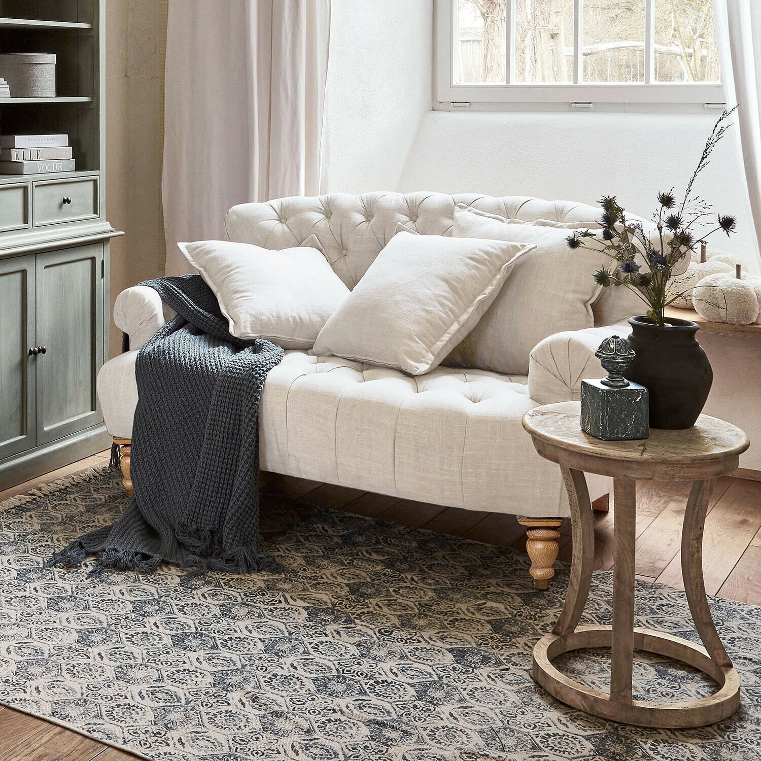 Divano Springfield Village Divano beige trapuntato in lino con cuscini e coperta grigia lavorata a maglia in soggiorno accogliente con tavolino in legno