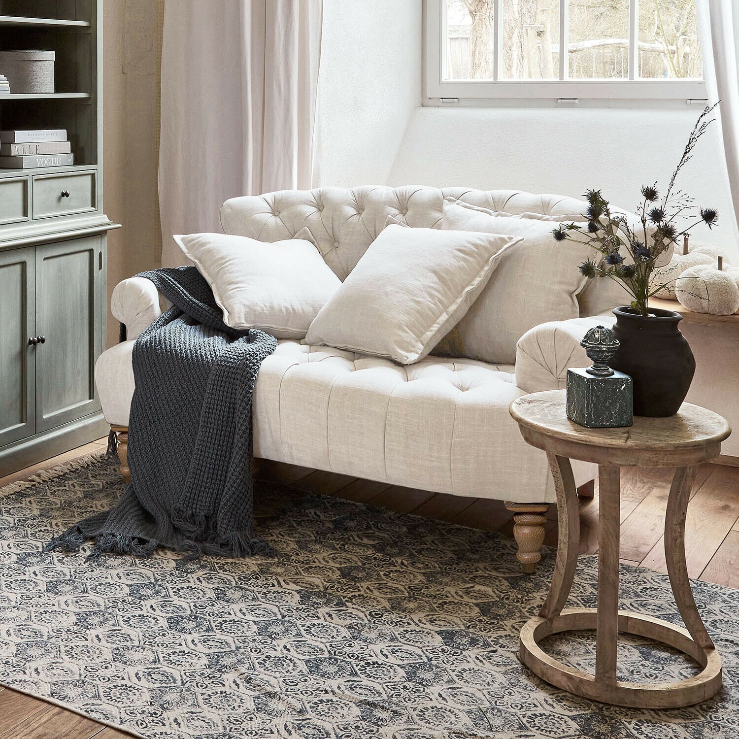 Divano Springfield Village Divano beige trapuntato in lino con cuscini e coperta grigia lavorata a maglia in soggiorno accogliente con tavolino in legno