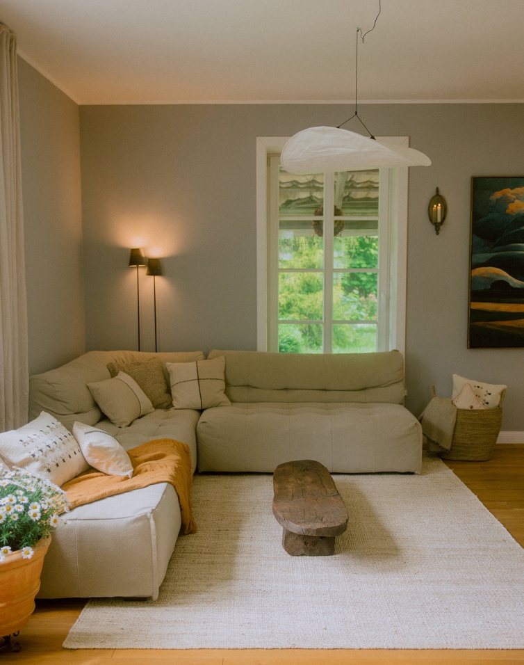 Soggiorno accogliente con divano ad angolo beige, tavolino in legno rustico e tappeto naturale in stile scandinavo