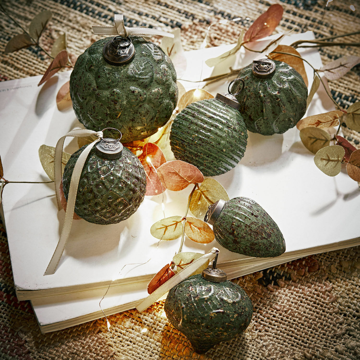 Set di 6 decorazioni natalizie Moriches Set di decorazioni natalizie verdi con texture e nastri su libro bianco su tappeto naturale
