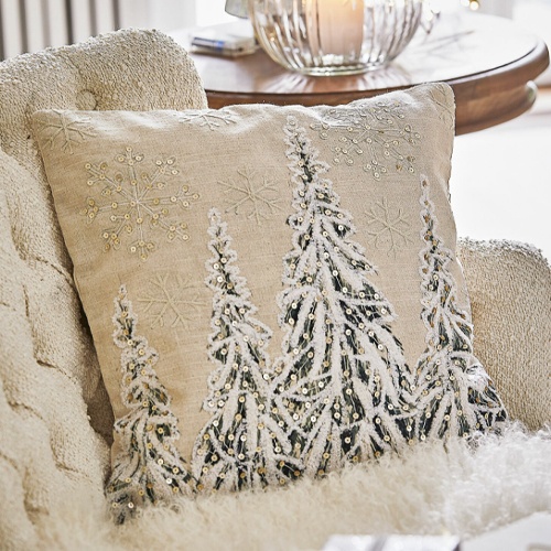 Cuscino decorativo beige con ricami di fiocchi di neve e alberi su poltrona morbida