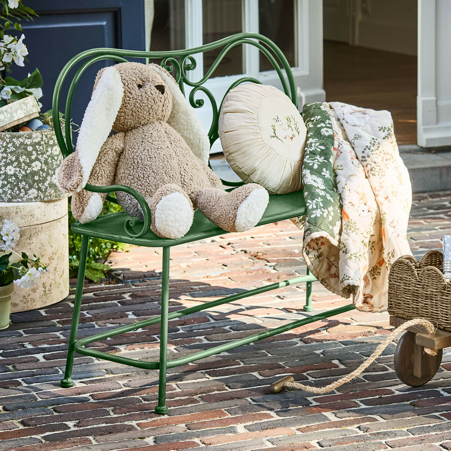 Banca Fernwick Panchina in metallo verde con coniglio di peluche beige e coperta floreale su patio in mattoni