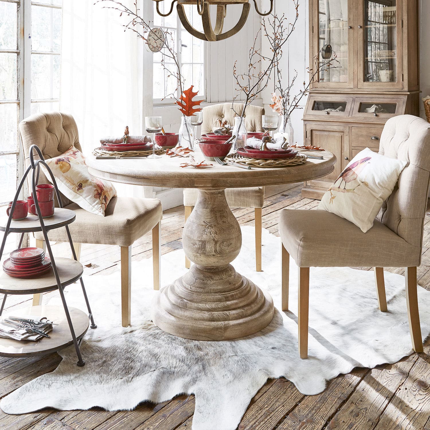 Tavolo Orlin Tavolo rotondo in legno chiaro con sedie imbottite beige e stoviglie rosse in sala da pranzo luminosa