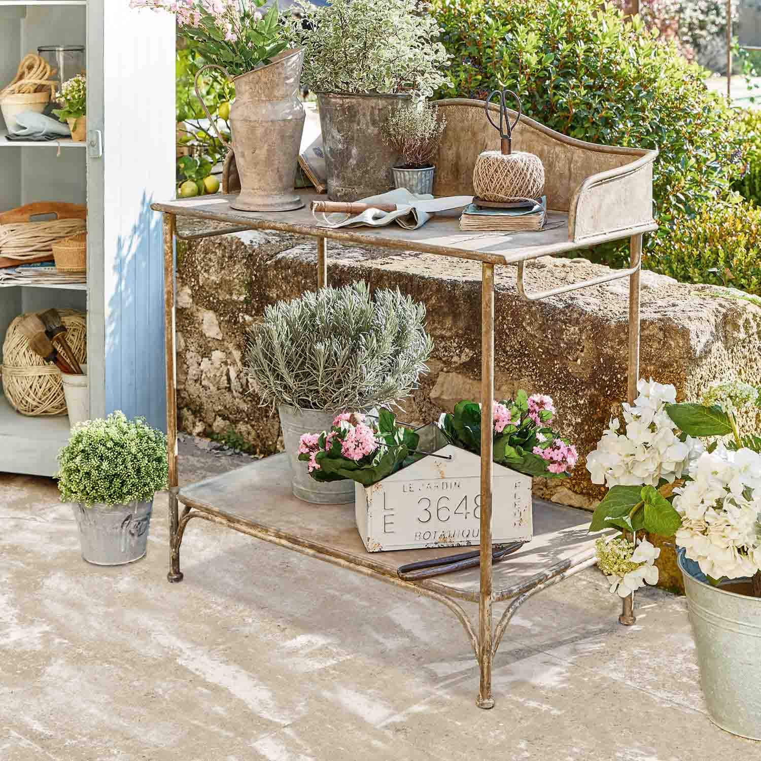 Tavolo da giardino in metallo con vasi decorativi e fiori in ambiente naturale soleggiato