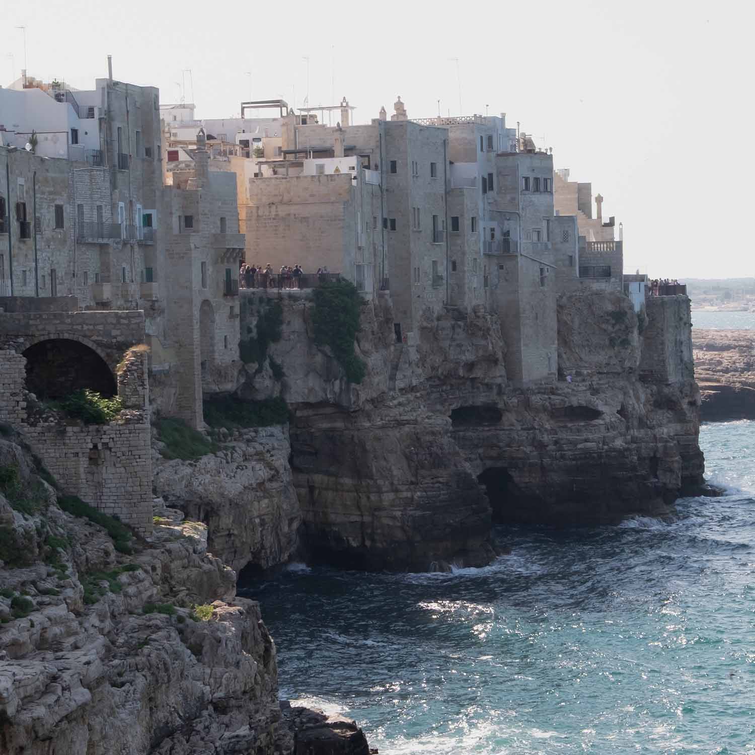 Vecchie case in pietra su scogliera sul mare con turisti e onde sulla costa