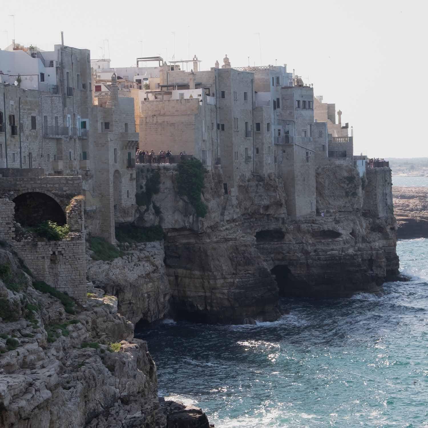 Vecchie case in pietra su scogliera sul mare con turisti e onde sulla costa