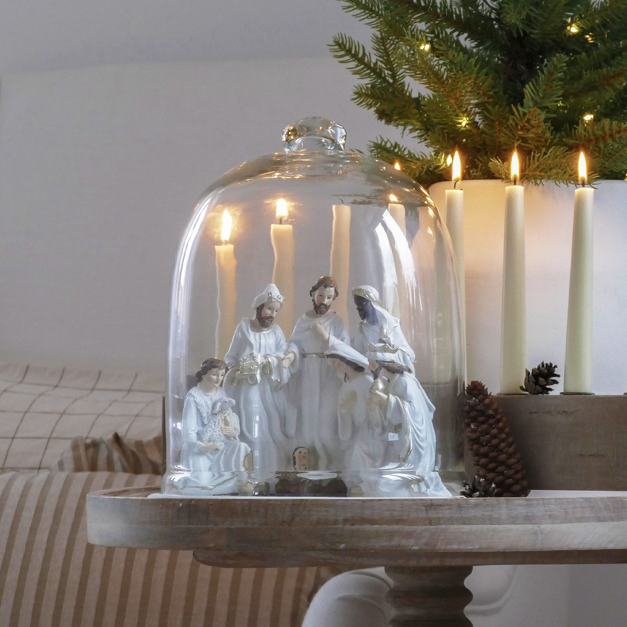 Presepe in ceramica bianca sotto campana di vetro con candele accese e decorazioni natalizie