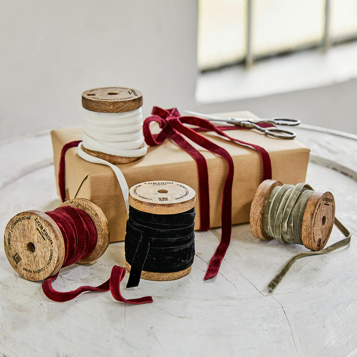 Set di 4 nastri di velluto Hilary Set di bobine in legno con nastri di velluto bianco, rosso, nero e oliva su tavolo con regalo