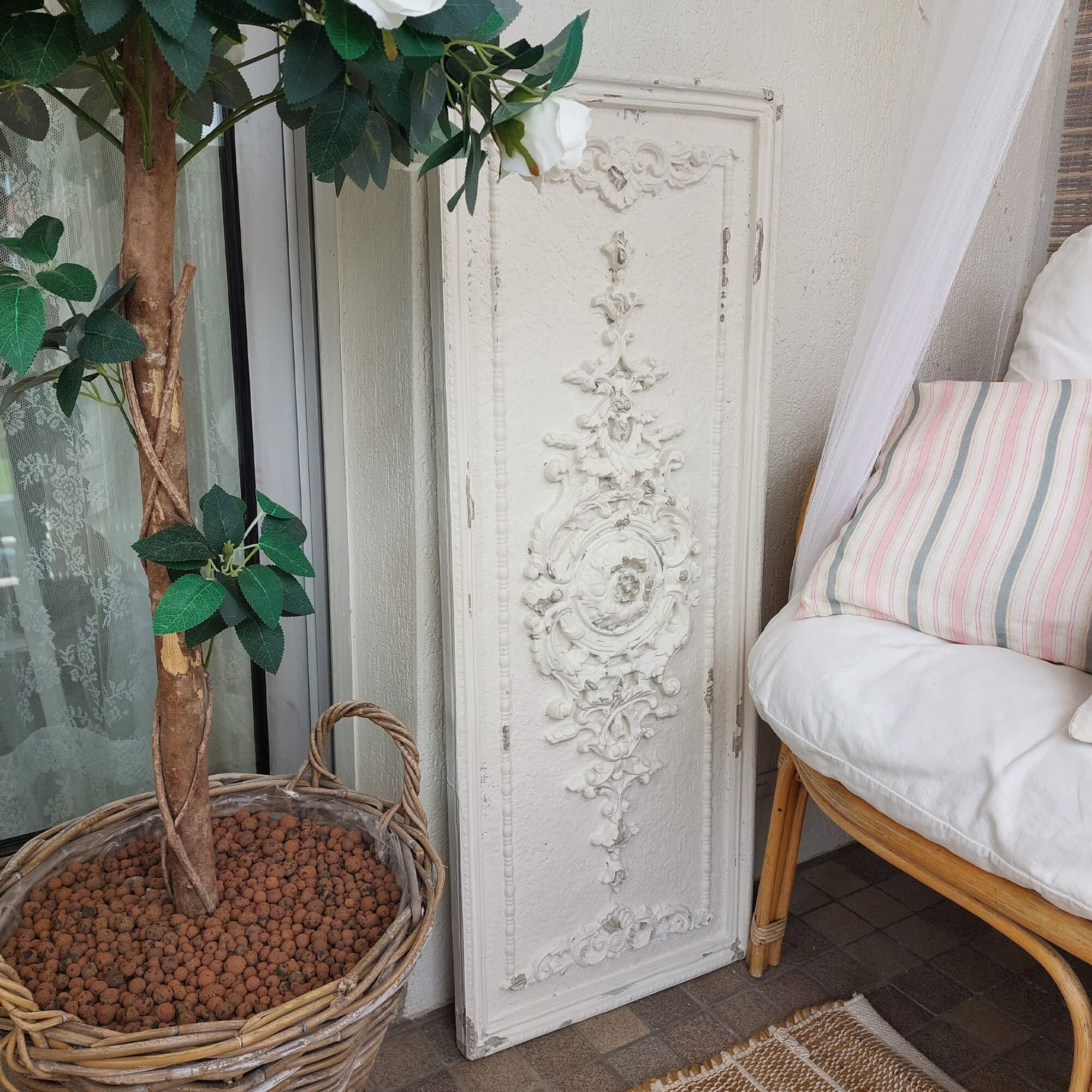 Pannello decorativo bianco con ornamento vintage accanto a un cesto di vimini con pianta