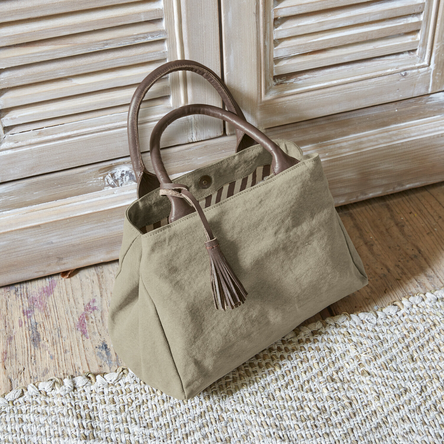Borsa Hoya Borsa beige in tessuto con manici in pelle marrone e nappina su pavimento in legno