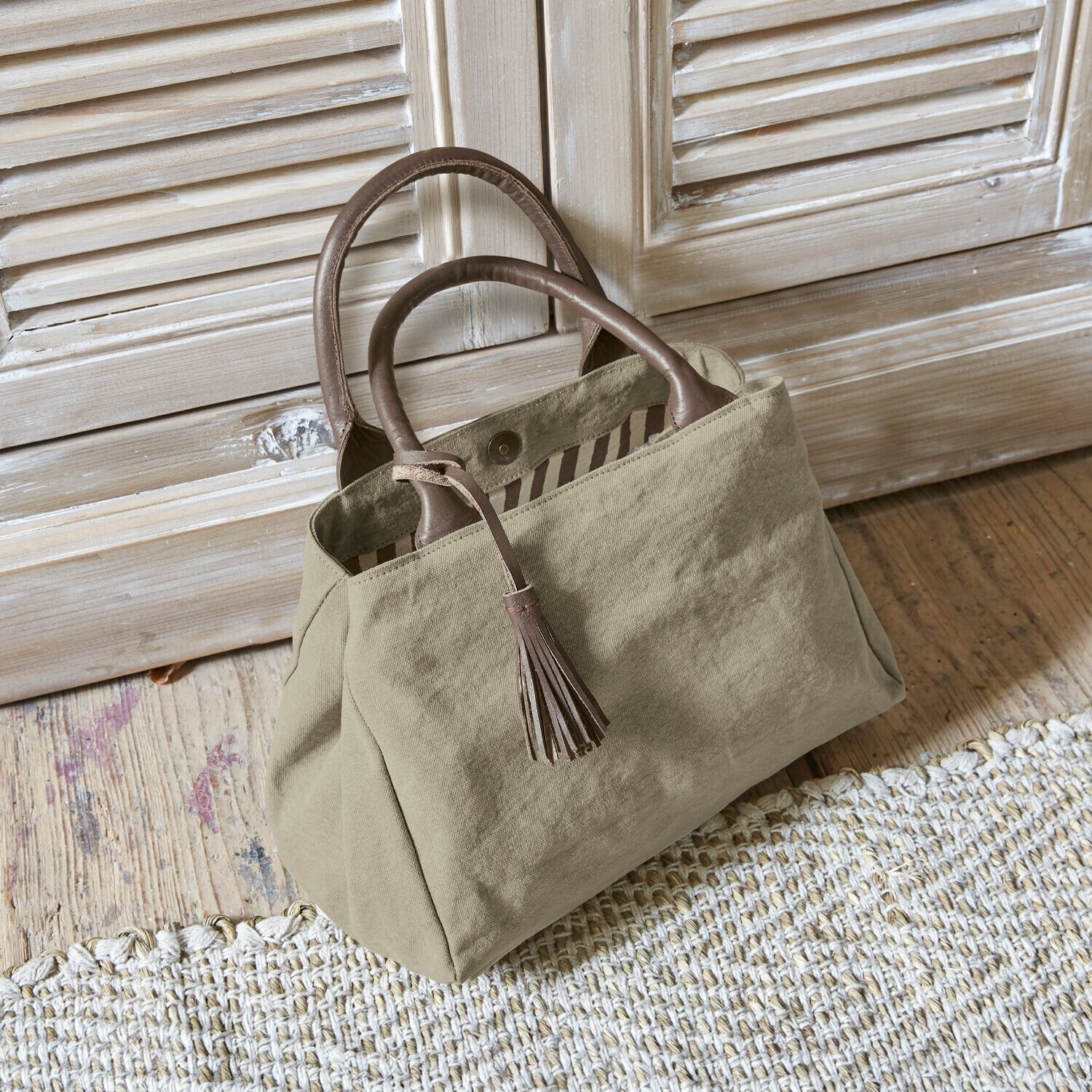 Borsa Hoya Borsa beige in tessuto con manici in pelle marrone e nappina su pavimento in legno