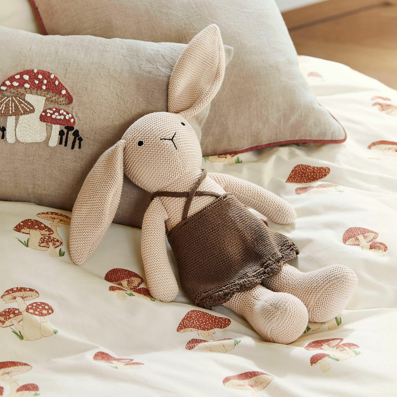Peluche Flicka Coniglio lavorato a maglia beige con vestito marrone su biancheria da letto con stampa di funghi, cuscino decorativo