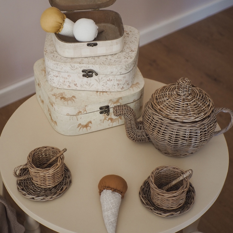 Set da tè per bambini in vimini con teiera e tazze su tavolo rotondo beige
