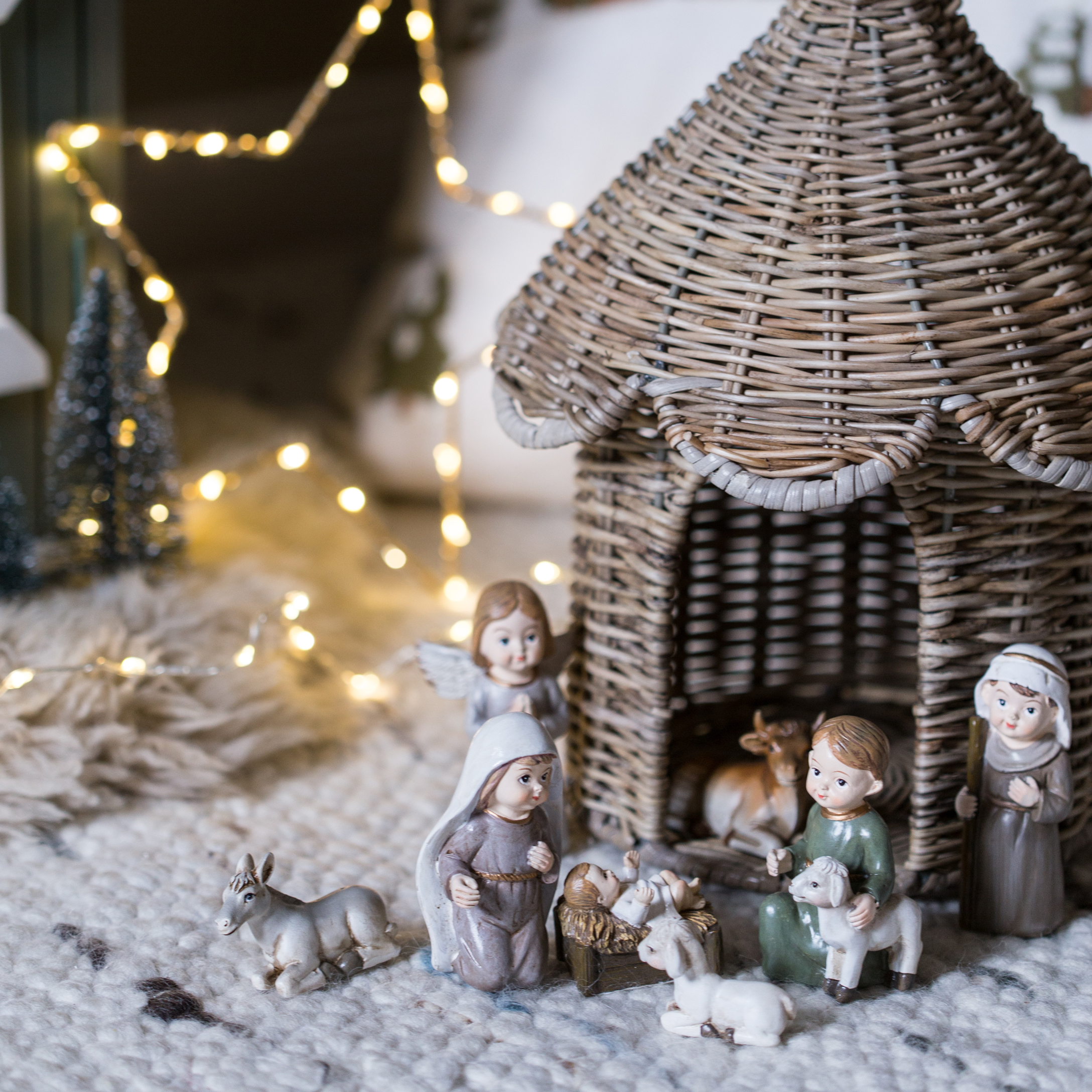 Figure del presepe natalizio con casetta in vimini e personaggi su tappeto morbido con luci LED