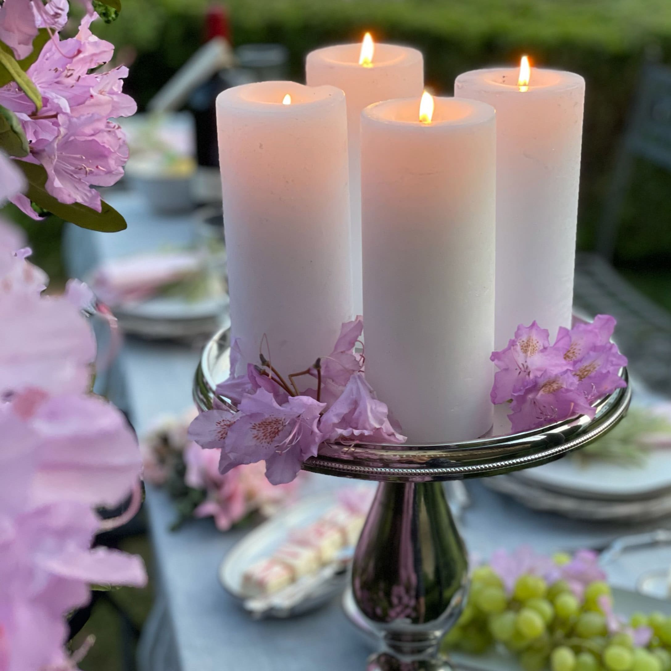 Quattro candele bianche su portacandele d'argento con fiori rosa su tavolo da giardino