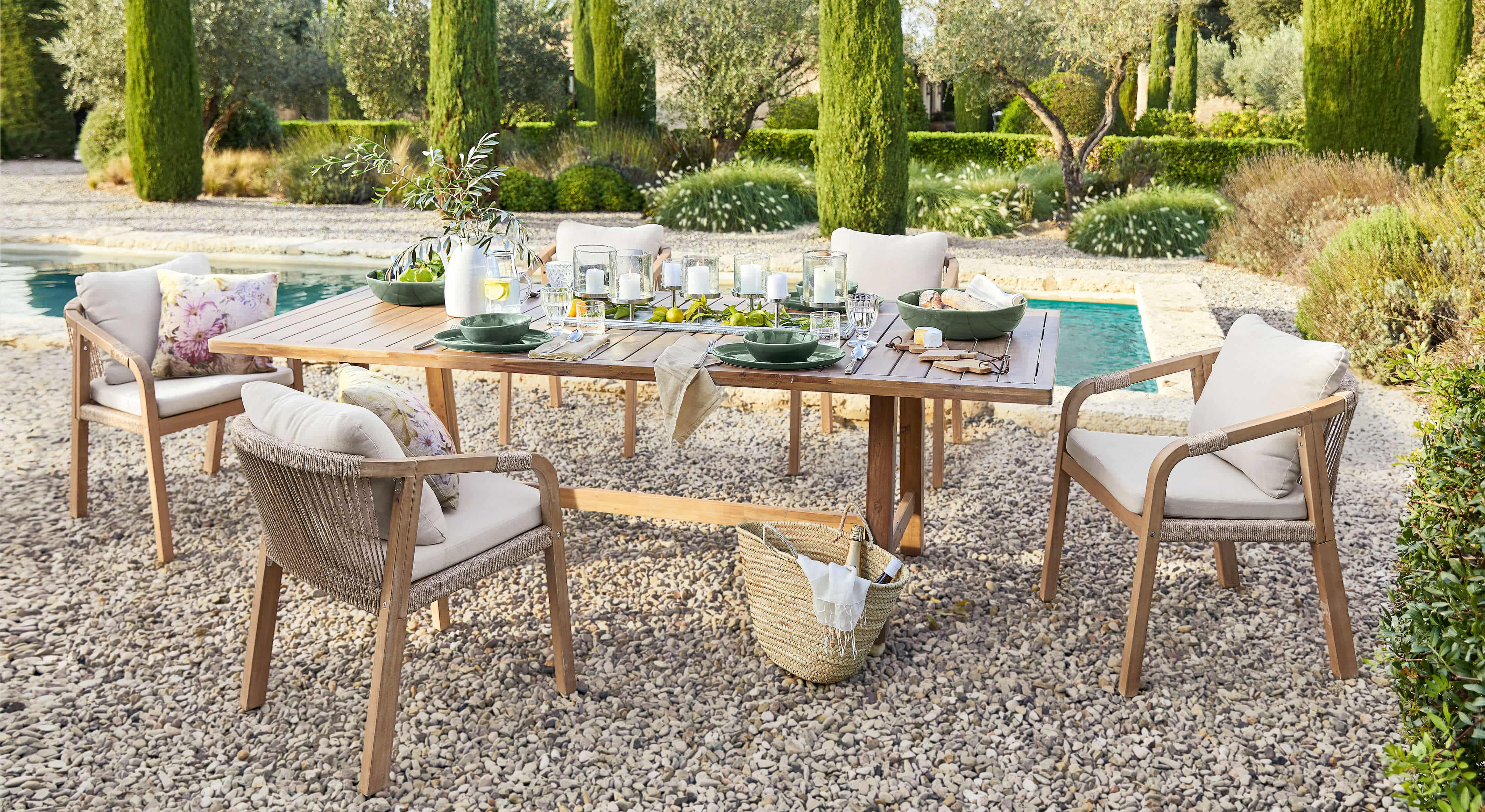 Set di mobili da giardino con tavolo in legno e sedie beige su patio di ghiaia vicino alla piscina
