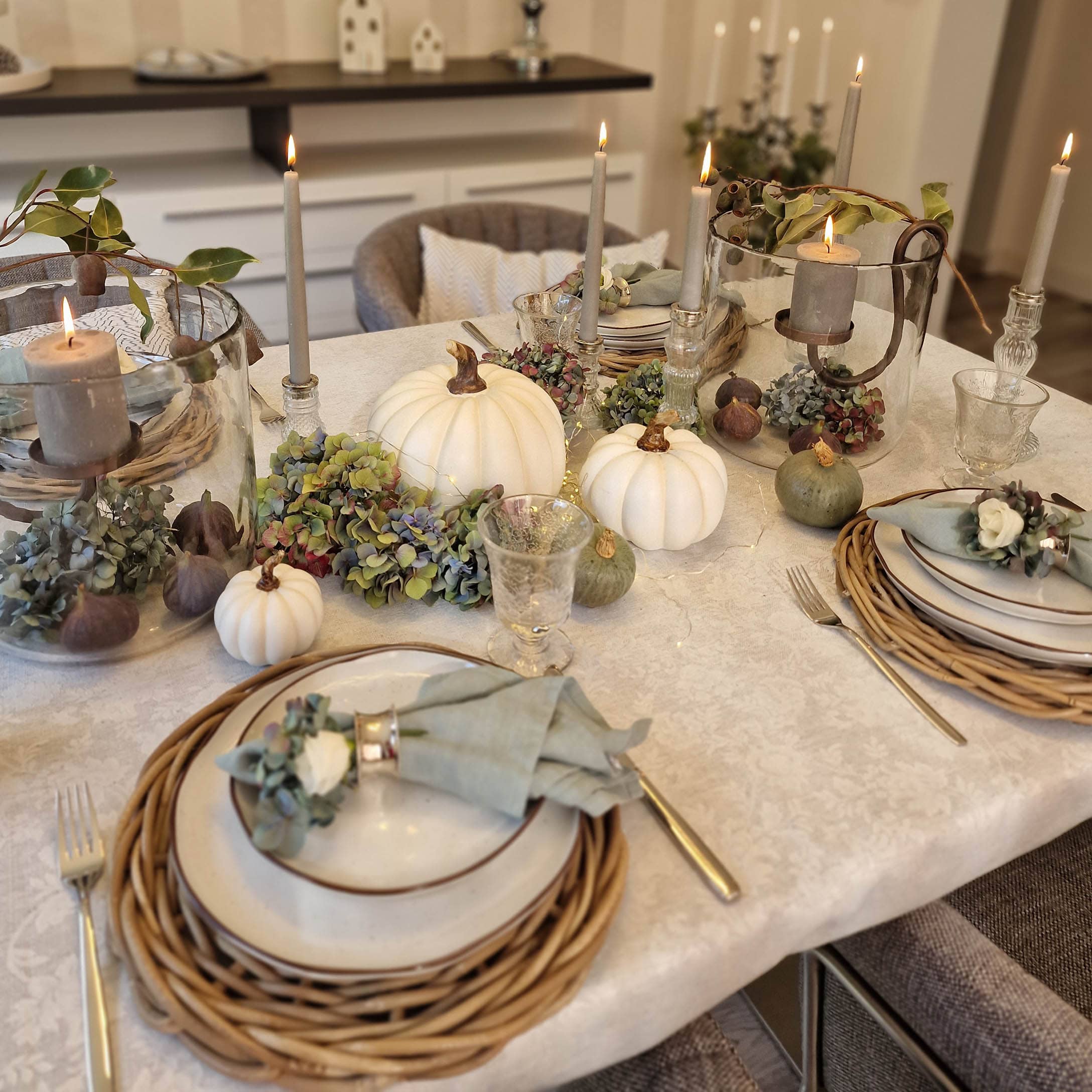 Elegante decorazione autunnale da tavola con zucche bianche, candele e elementi naturali su tovaglia