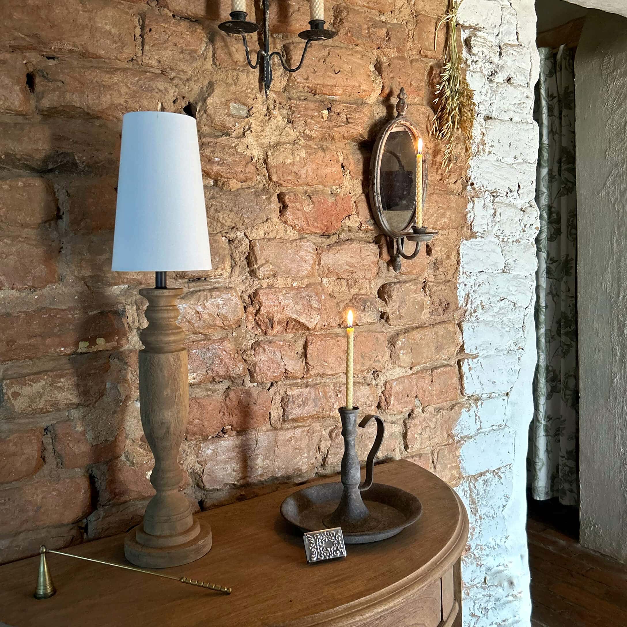Lampada in legno con paralume bianco e portacandele in metallo con candela accesa su tavolo in legno vicino a muro di mattoni