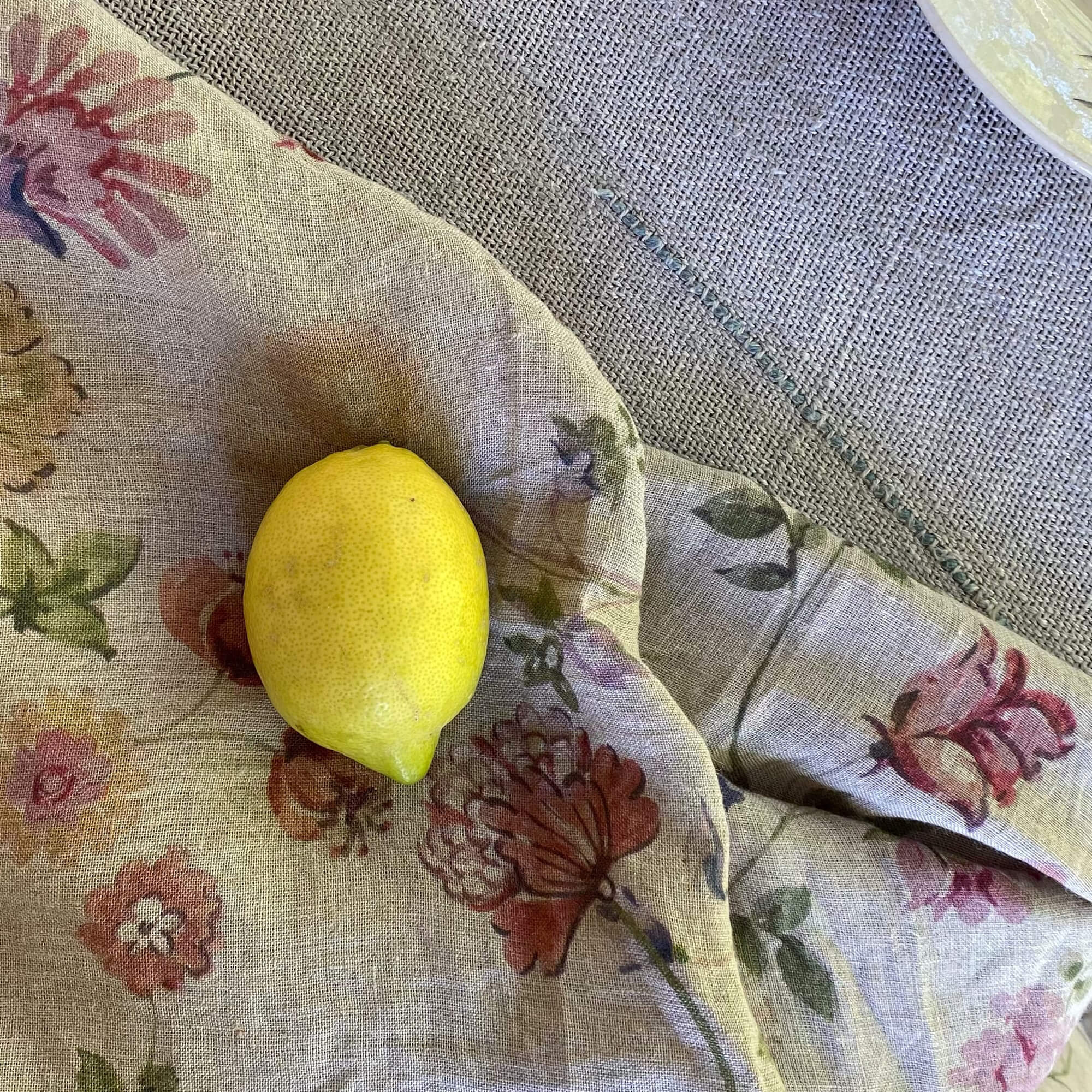 Tovaglia di lino con motivo floreale dai toni caldi e un limone giallo sopra