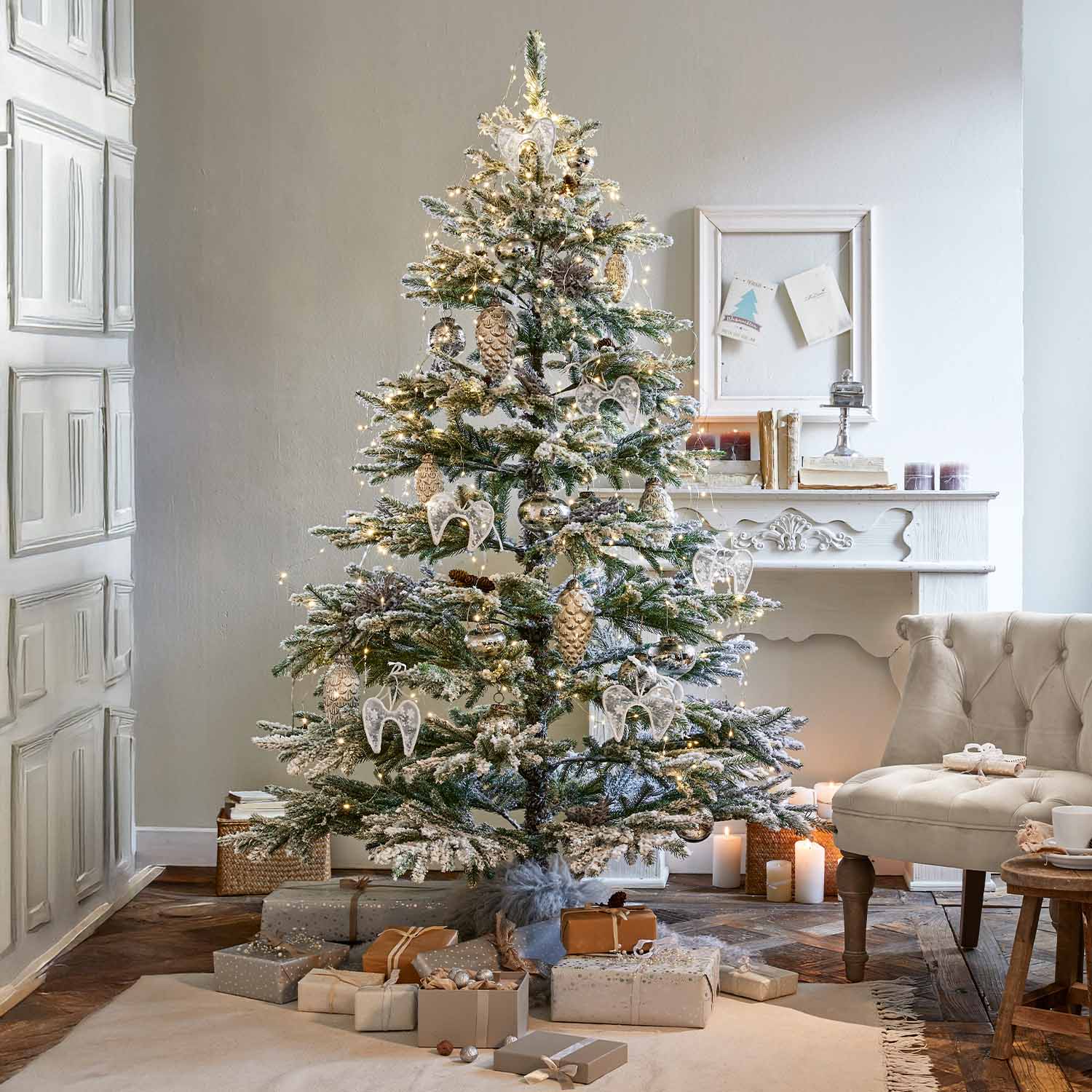 Albero di Natale innevato con decorazioni bianche e dorate e regali in un soggiorno accogliente con camino