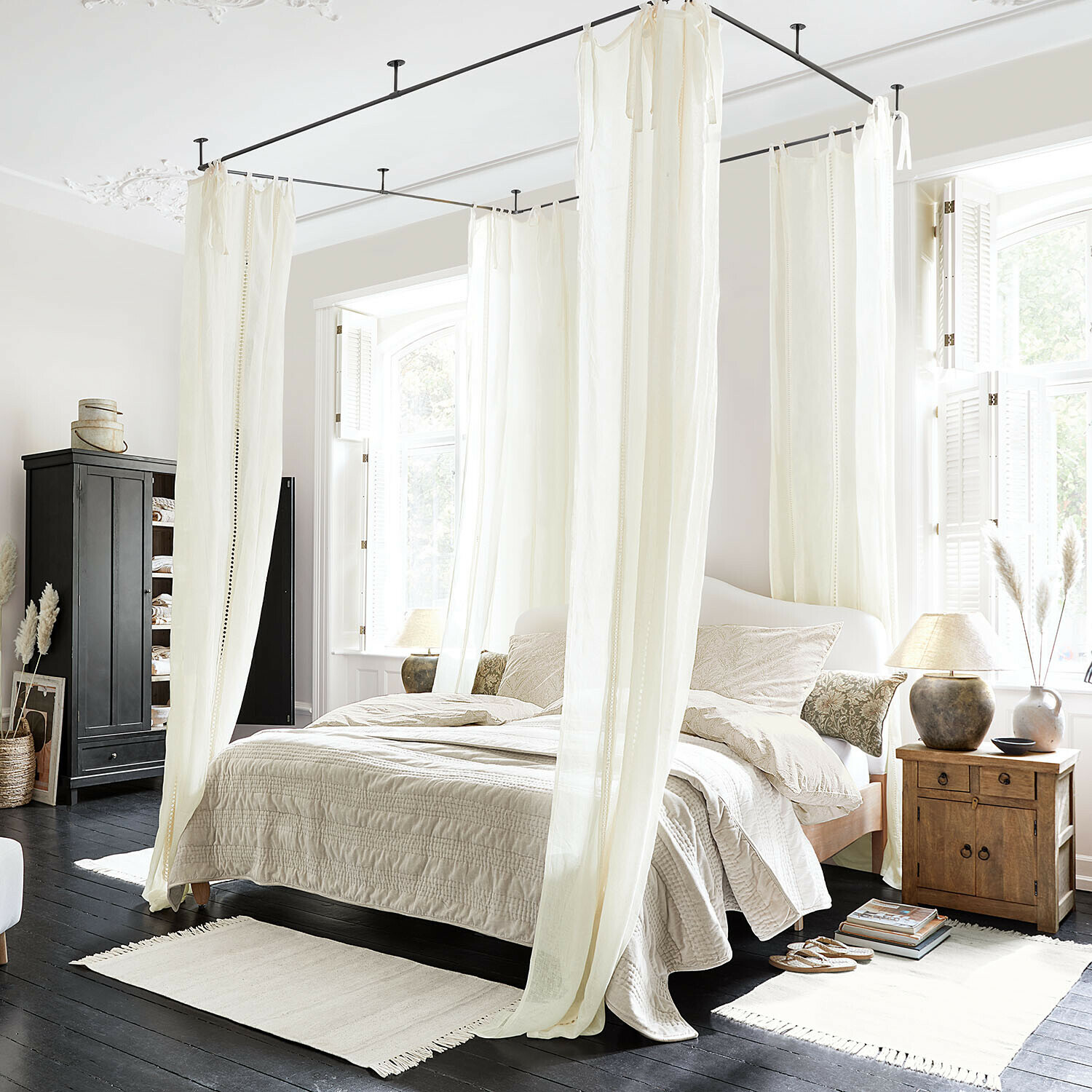 Tenda Elorine Camera da letto con letto a baldacchino in cotone bianco e biancheria beige su pavimento in legno scuro, luce naturale