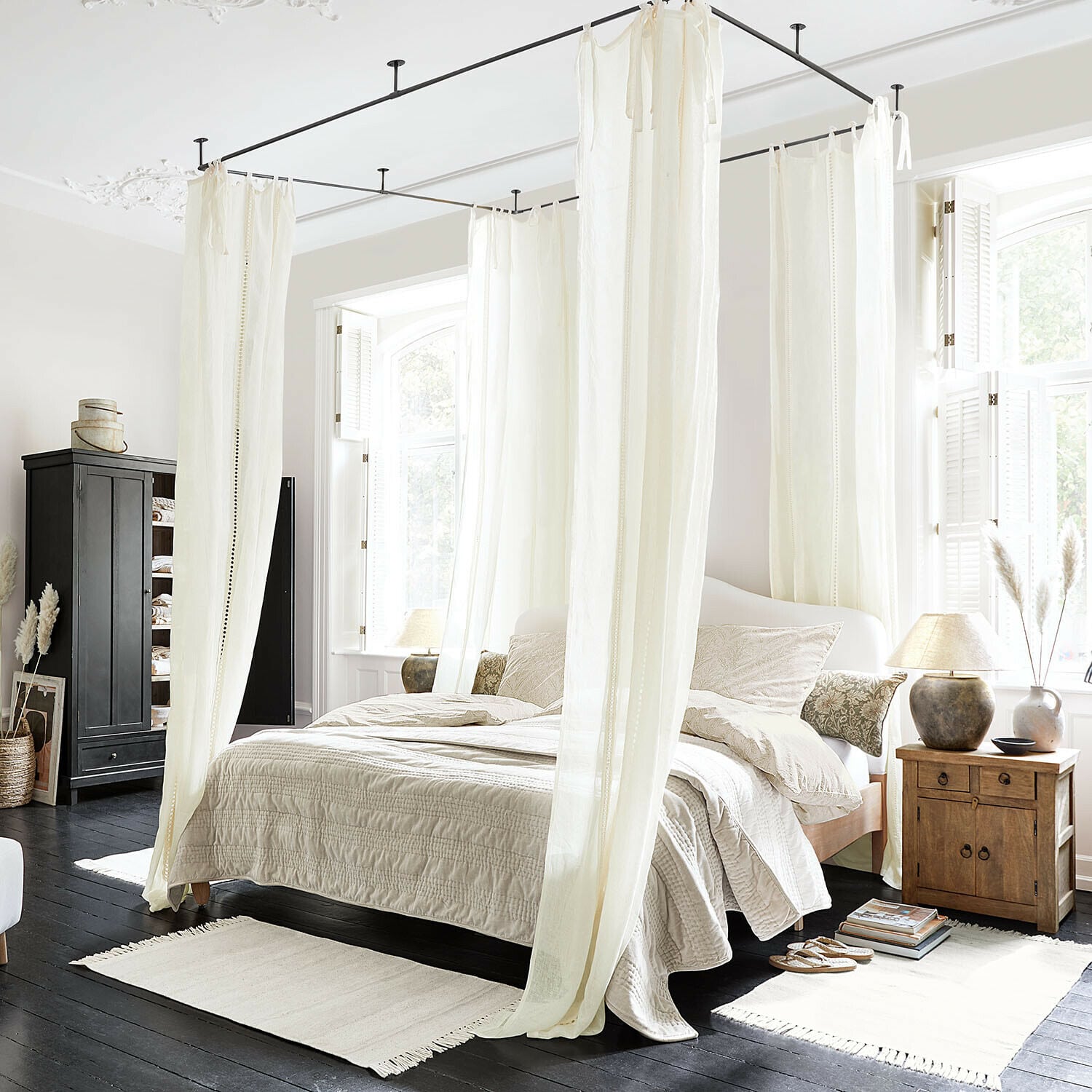 Tenda Elorine Camera da letto con letto a baldacchino in cotone bianco e biancheria beige su pavimento in legno scuro, luce naturale