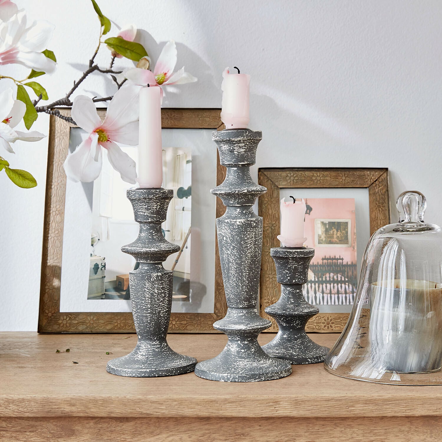 Set di 3 candelieri Ténébrelle Set di tre candelabri in legno grigio effetto invecchiato con candele rosa su tavolo in legno