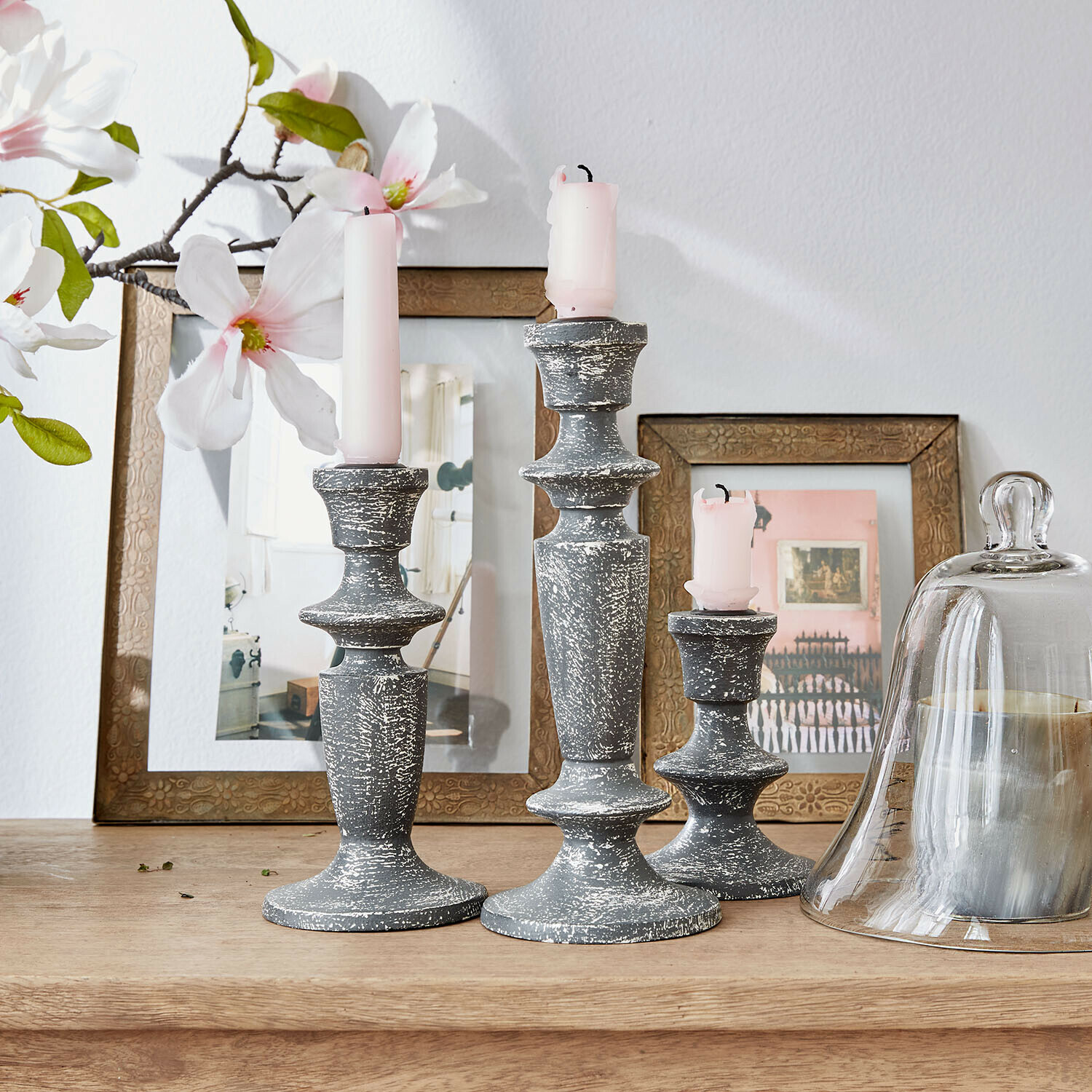 Set di 3 candelieri Ténébrelle Set di tre candelabri in legno grigio effetto invecchiato con candele rosa su tavolo in legno