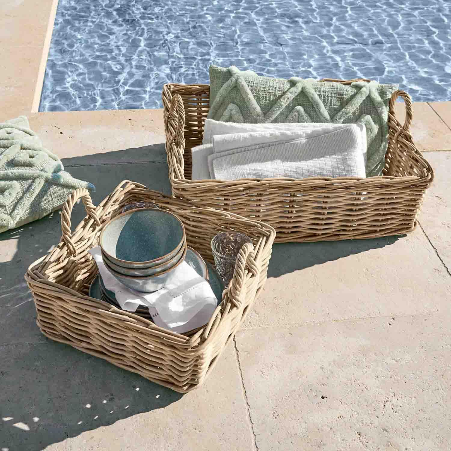 Due ceste di vimini con manici, con cuscini verdi e asciugamani bianchi, accanto alla piscina