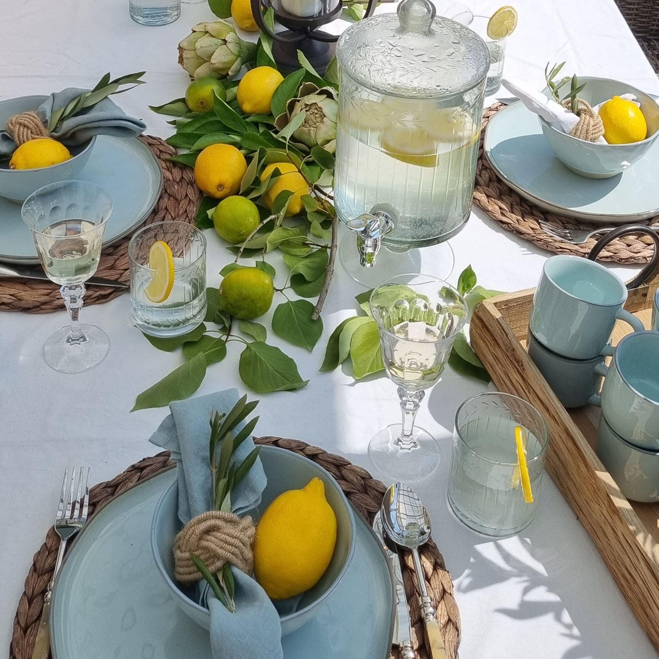 Tavola estiva con ceramica azzurra, limoni e foglie verdi su tovaglia bianca, decorazione tavola
